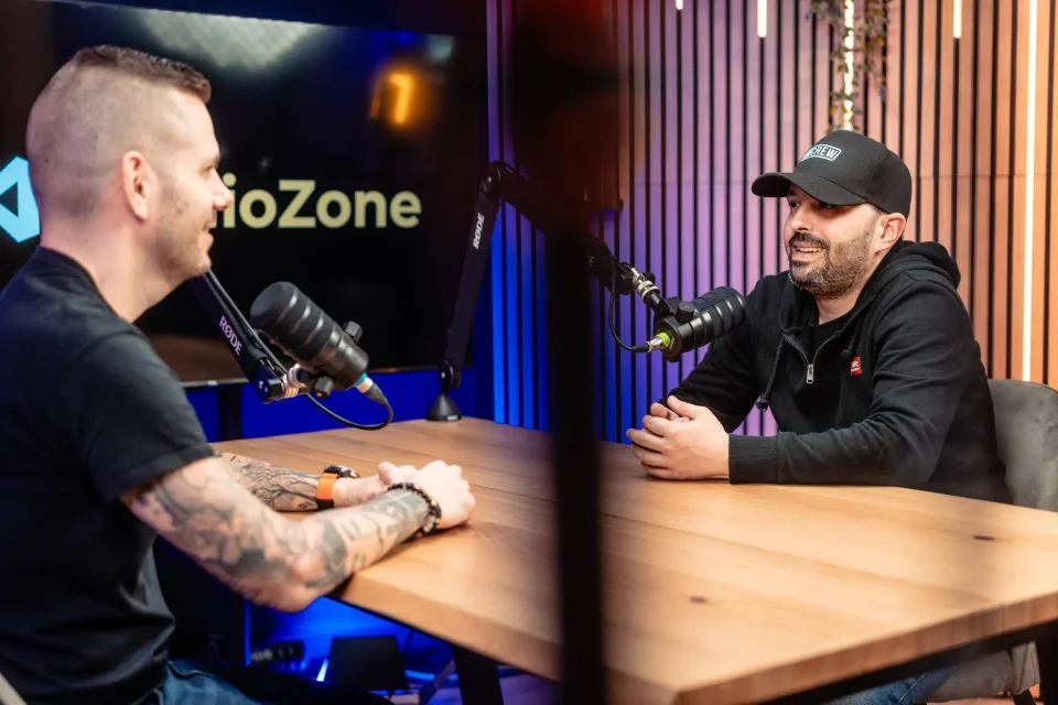 Podcast beszélgetés két résztvevővel a Zóne stúdióban, asztali mikrofonokkal és meleg-kék világítással