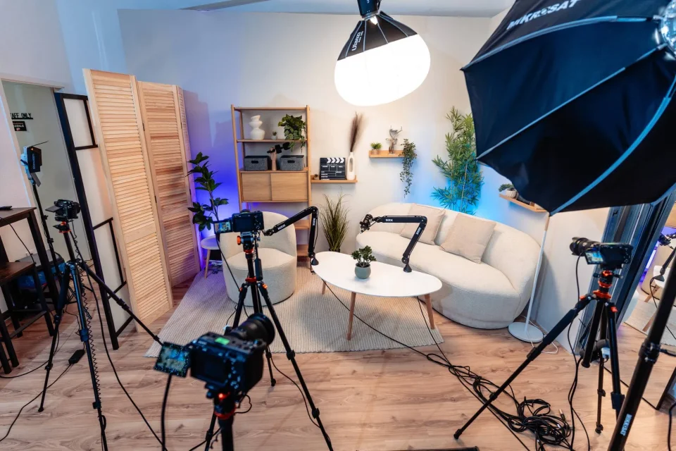 Skandináv stúdió világos enteriőrje bézs kanapéval, kamera-állványokkal és softbox lámpával