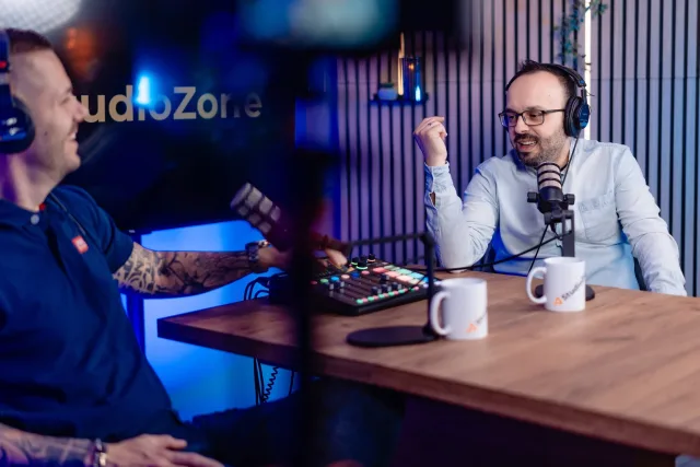 Két beszélgető az asztalnál fejhallgatóval, Rodecaster keverővel és StudioZone képernyővel