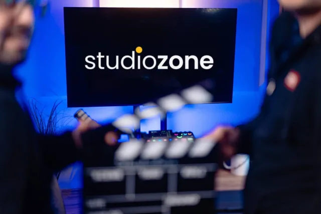 A studiozone logó a nagy kijelzőn, előtérben elmosódott mikrofon és csapótábla