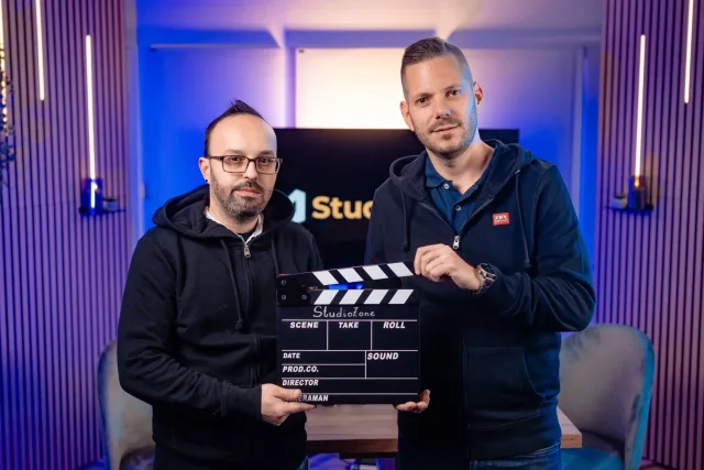 Két műsorvezető StudioZone csapótáblával, lila LED-es faléces háttér előtt
