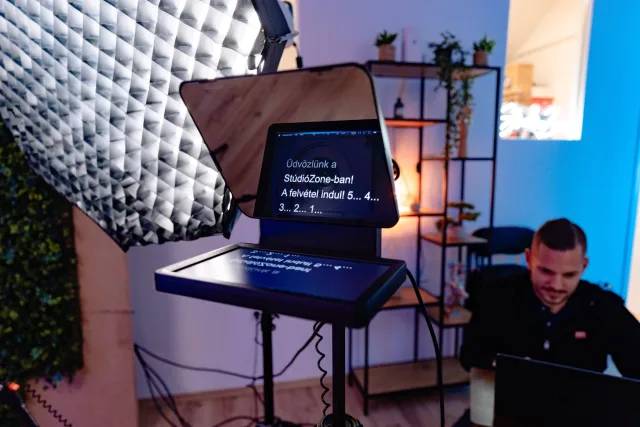 Teleprompter visszaszámlálóval és akusztikus habpanel a stúdióban, laptopnál ülő operátor