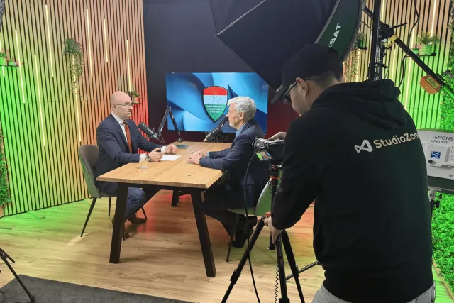 Élő forgatás a stúdióban: két öltönyös vendég és a StudioZone operatőre, színes háttérfénnyel